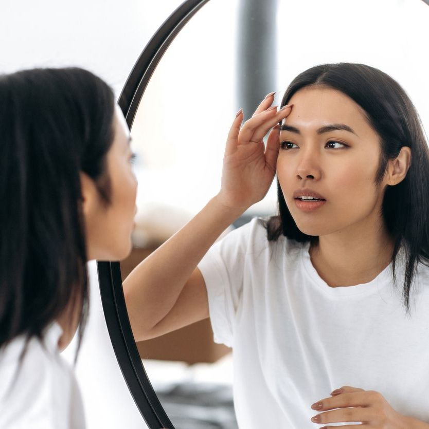 woman looking in mirror at her skin to see if she is due for dermaplaning