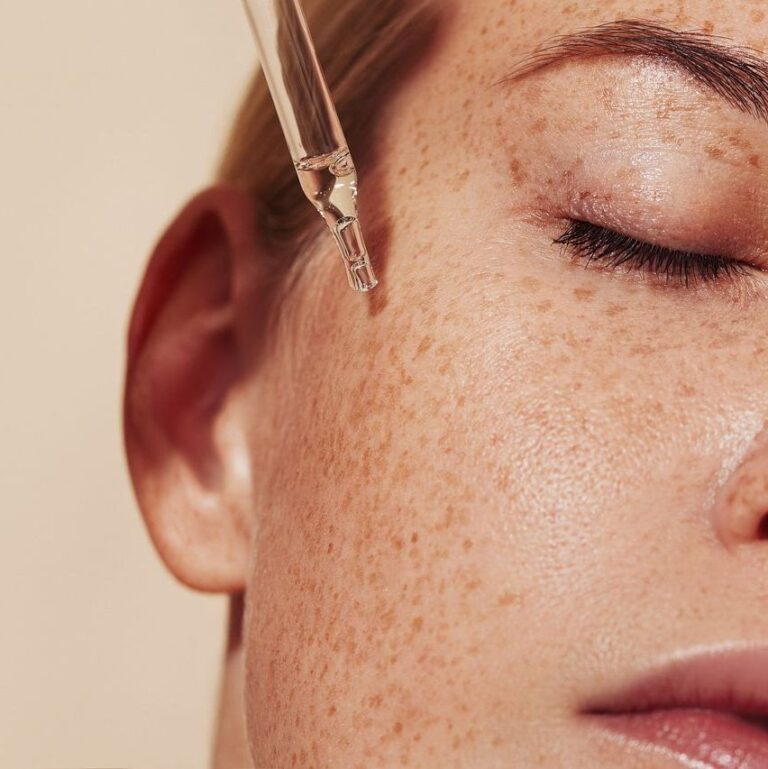 Close-up highly detailed shot of female skin with freckles and pipette with serum. Cropped shot of young woman with smooth perfect skin applying liquid serum on face.