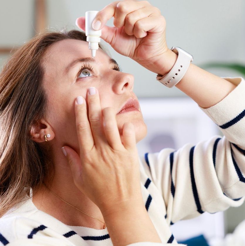 Young woman putting eye drops at home